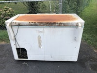 an old rusted white refrigerator sitting on the side of the road